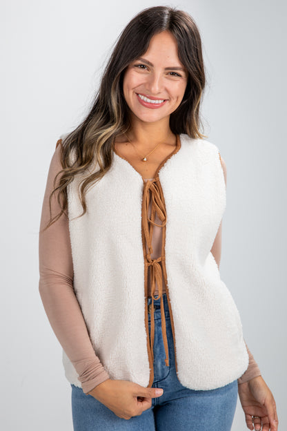 Woman wearing a white vest with brown buttons on a plain background
