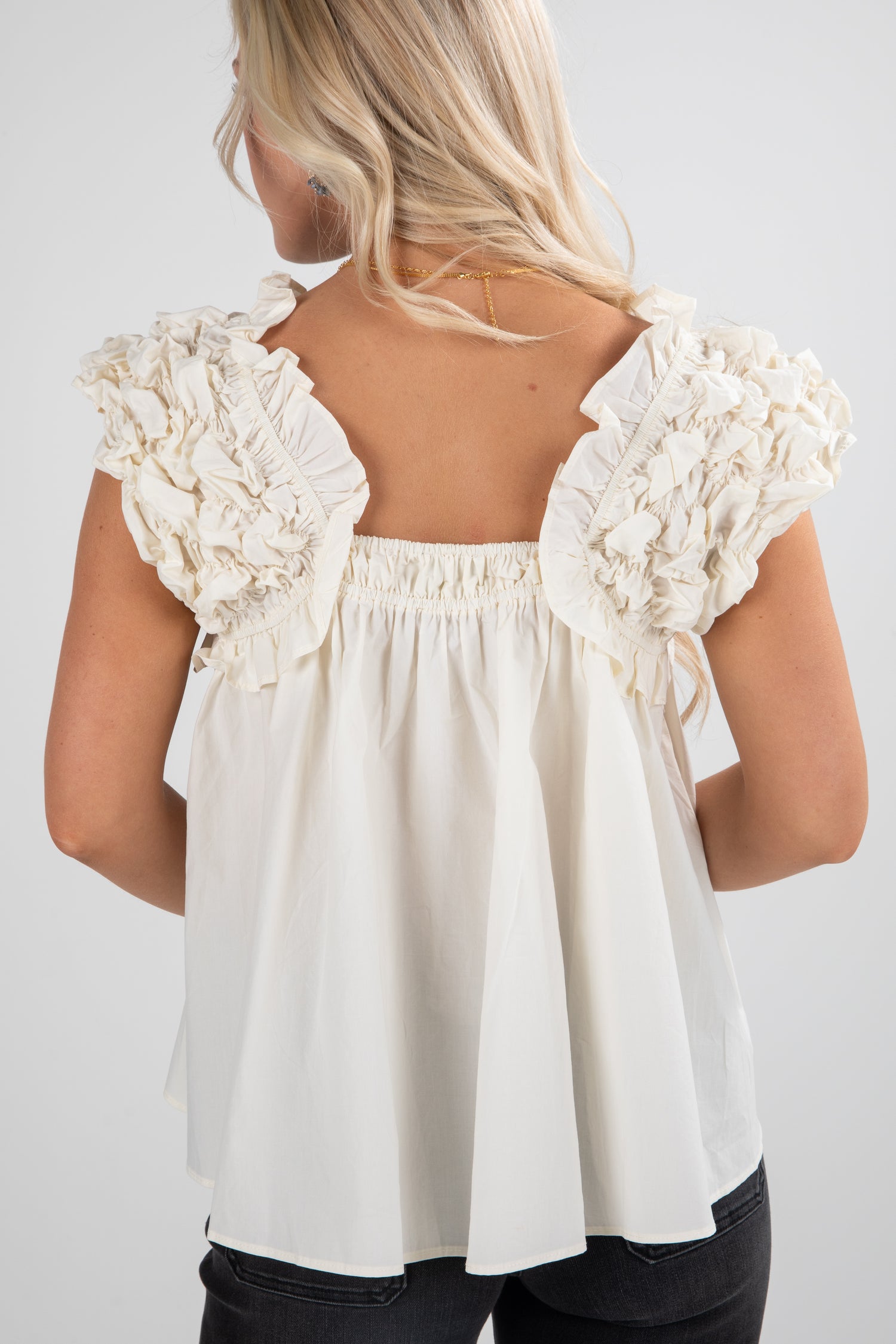 White blouse with ruffled shoulders on a plain background