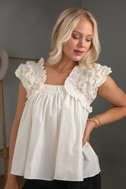Woman wearing a white blouse with ruffled details against a neutral background