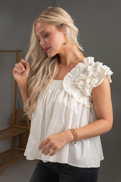 Woman wearing a white blouse with ruffled sleeves against a neutral background