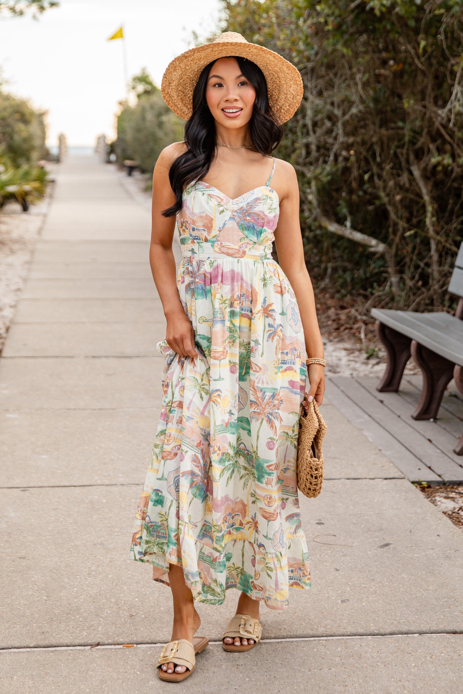 Woman in a floral dress and straw hat walking on a path with greenery.