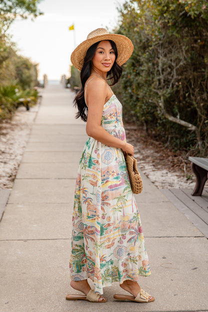 Woman in a floral dress and hat walking on a path with greenery.