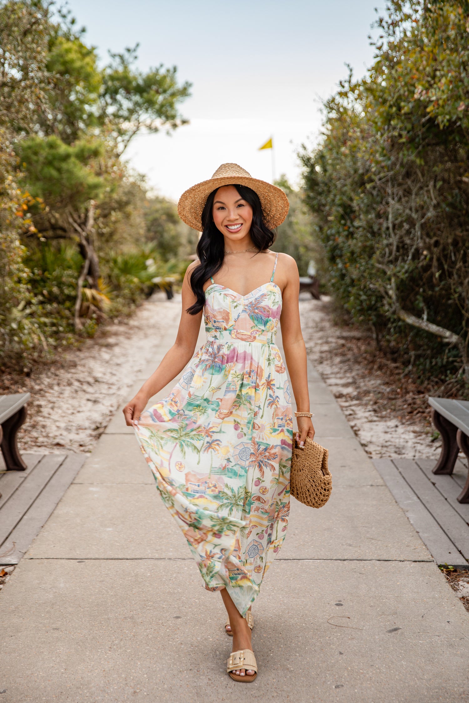Woman in a floral dress and straw hat walking on a path with greenery.