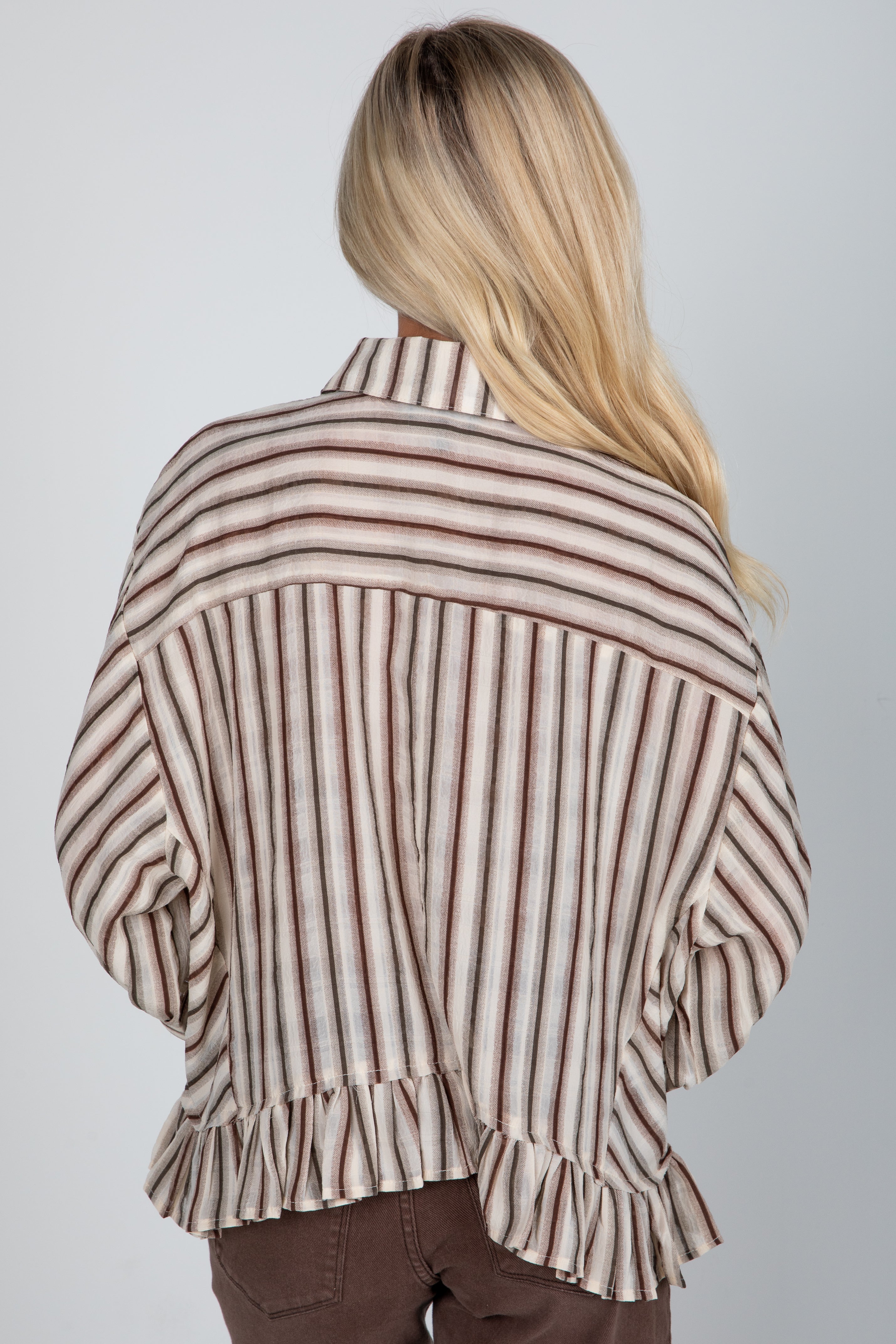 Person wearing a striped shirt with ruffled details on a plain background