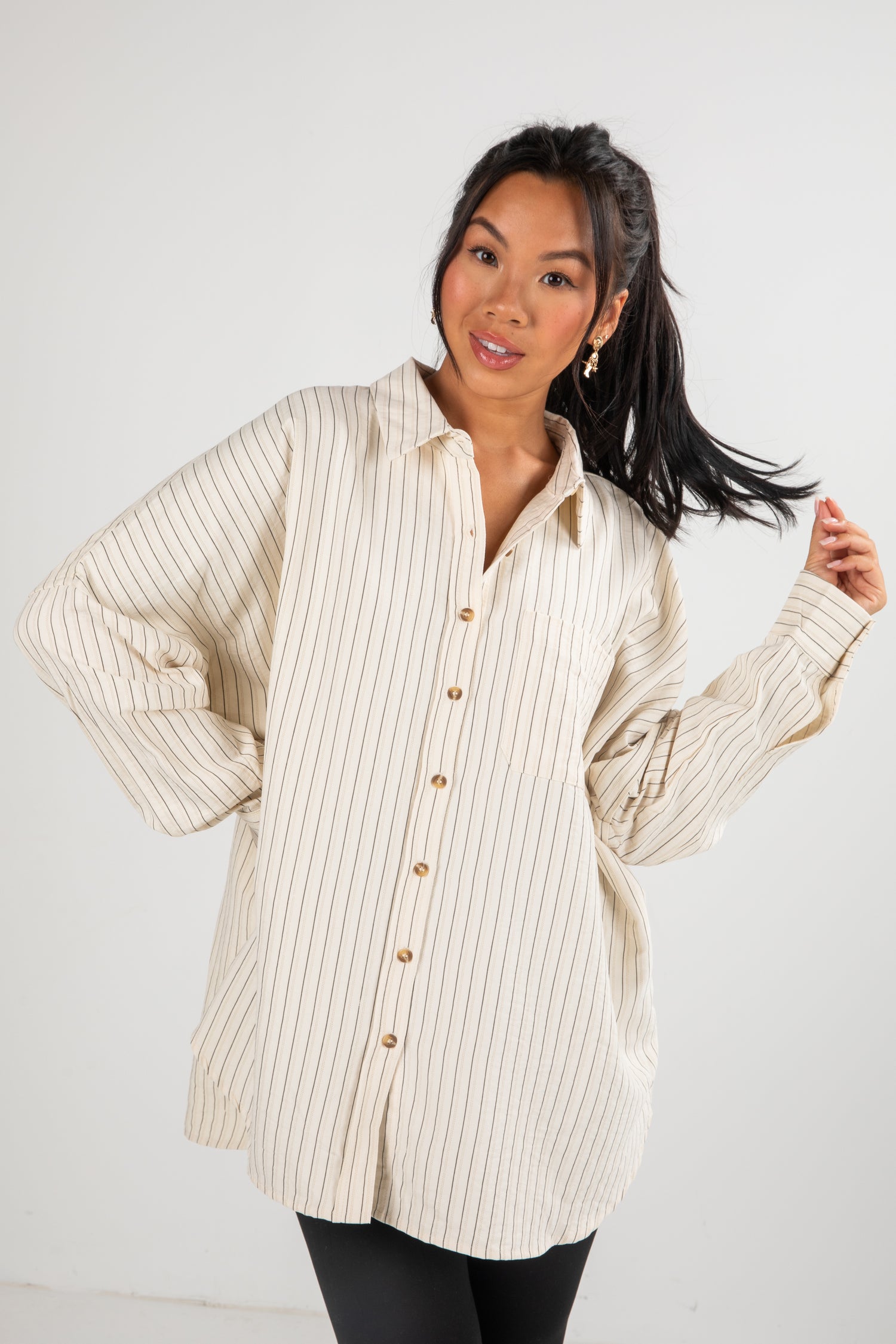 Woman wearing a beige ribbed sweater over a striped shirt on a white background