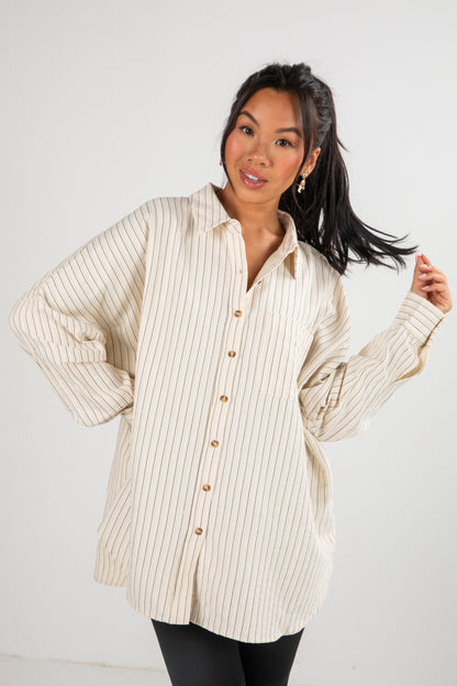 Woman wearing a beige ribbed sweater over a striped shirt on a white background