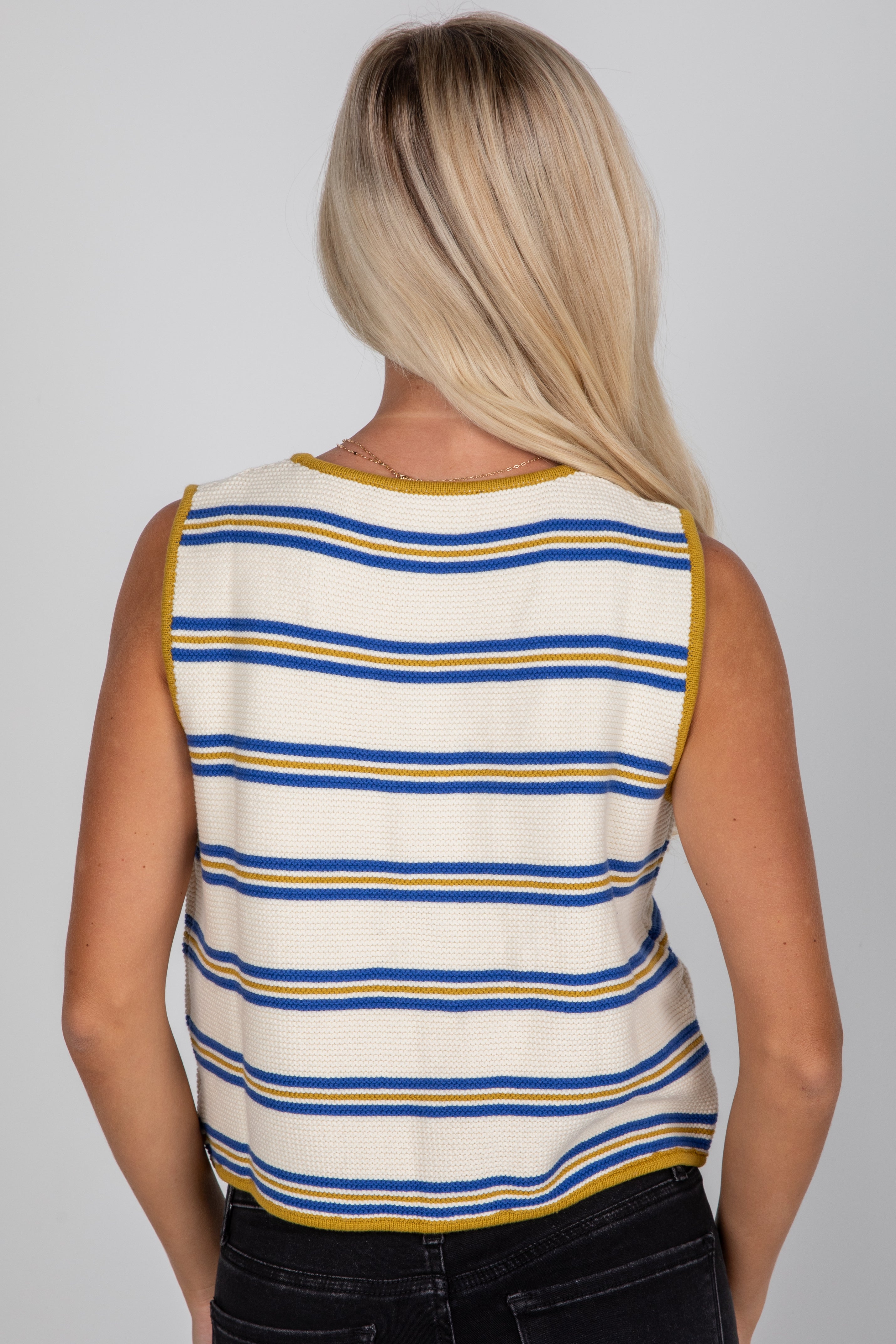Person wearing a sleeveless striped shirt with blue and yellow stripes on a gray background