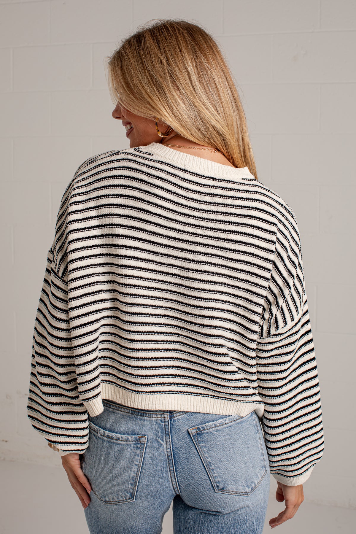 A woman shown from the back wearing a cropped knit sweater with thin horizontal black stripes on an off-white background, paired with light blue jeans.