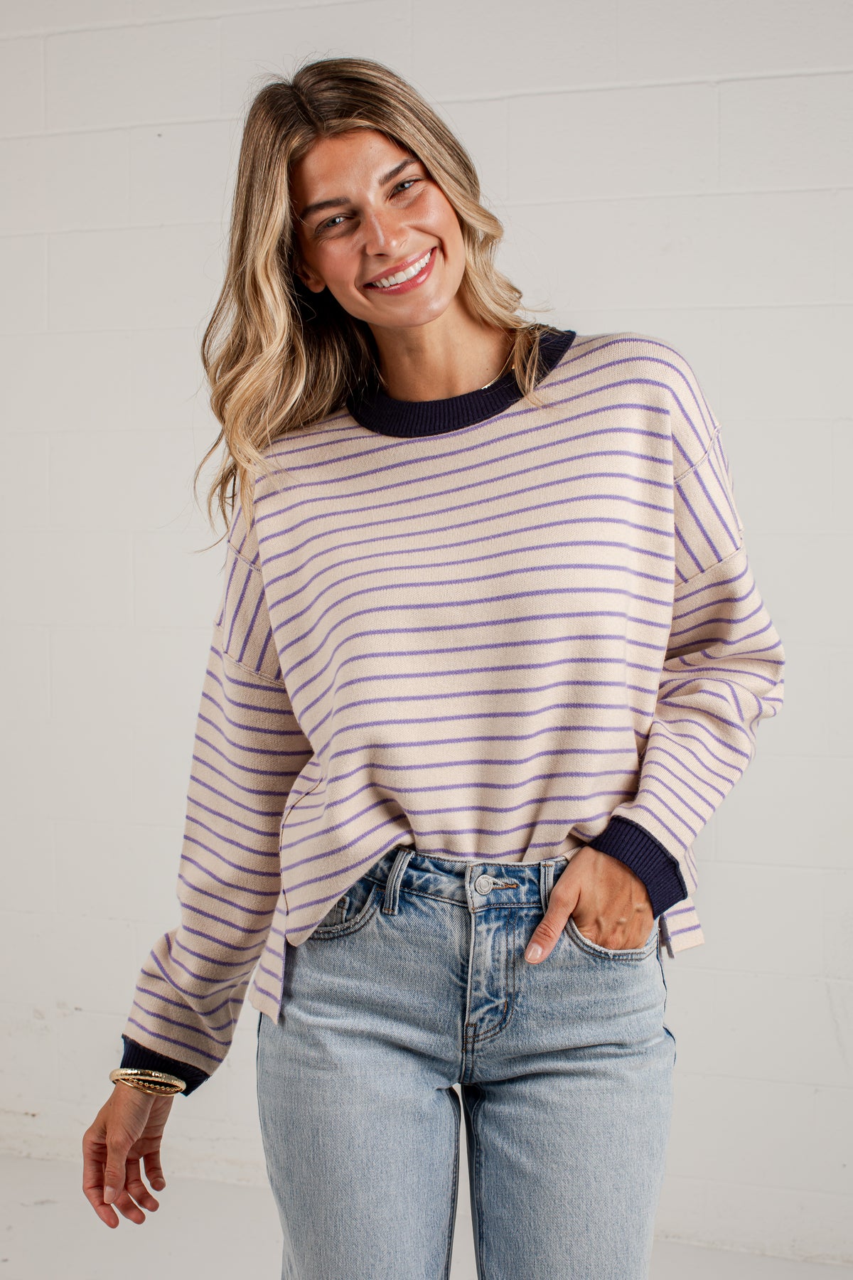 A woman wearing a light pink and navy blue horizontally striped long-sleeve knit top with dark navy ribbed collar, cuffs, and hem, paired with light-wash blue jeans.