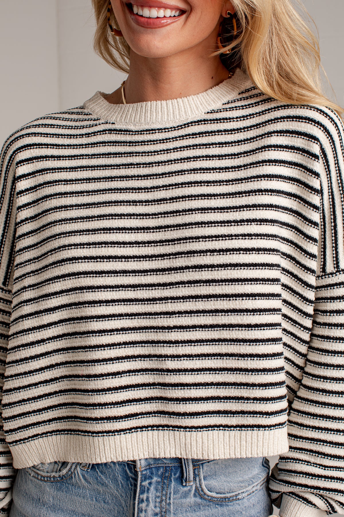 A close-up of a woman wearing a black and off-white horizontally striped knit sweater with blue jeans.