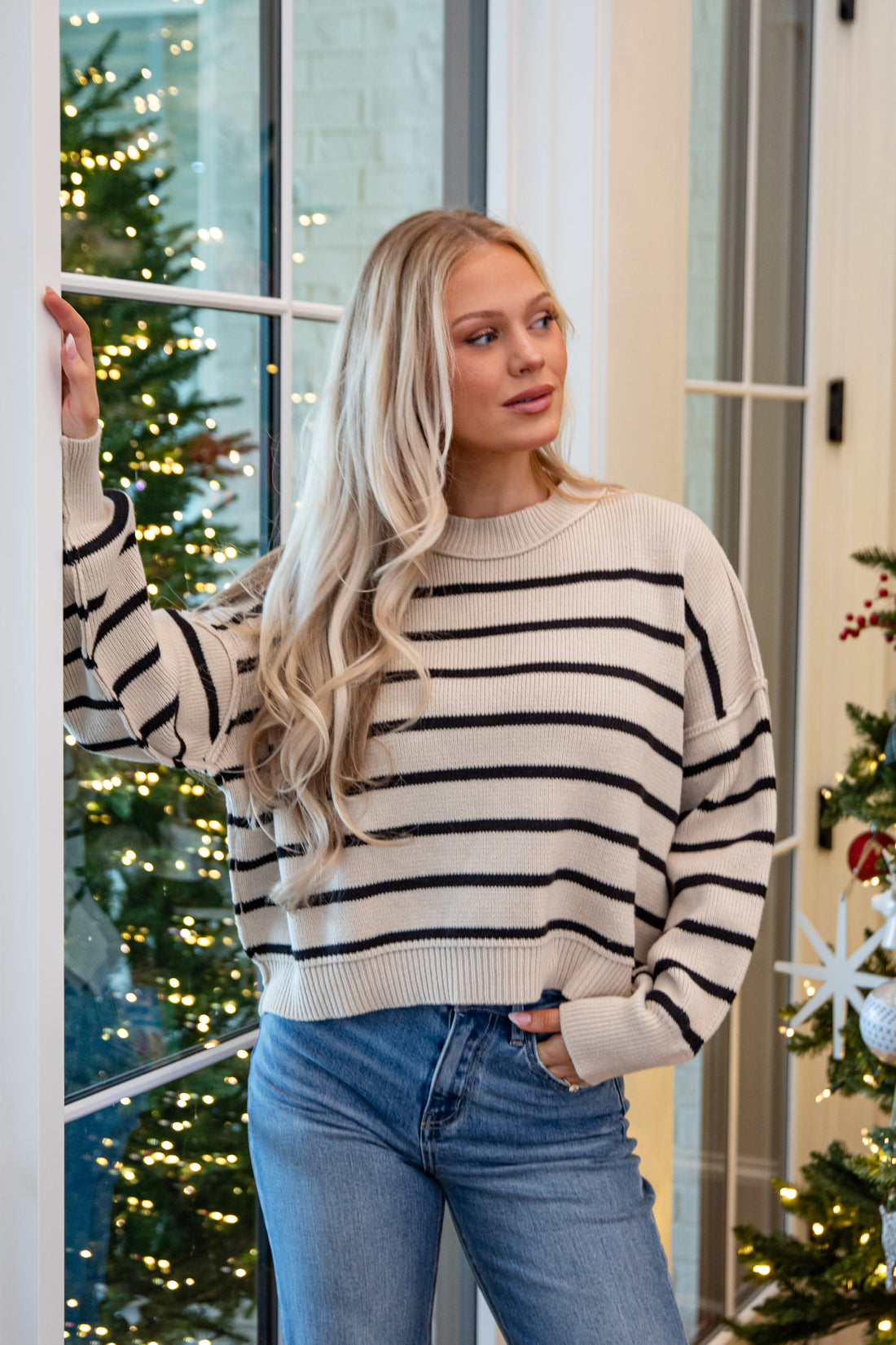 Woman wearing a striped sweater and jeans standing in front of a decorated Christmas tree.