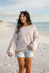 Woman standing on a sandy beach wearing a striped sweater and denim shorts.