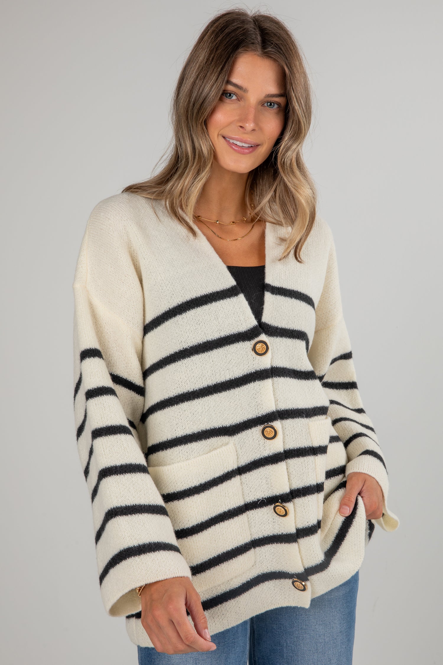 Woman wearing a cream and navy striped cardigan with gold buttons on a gray background