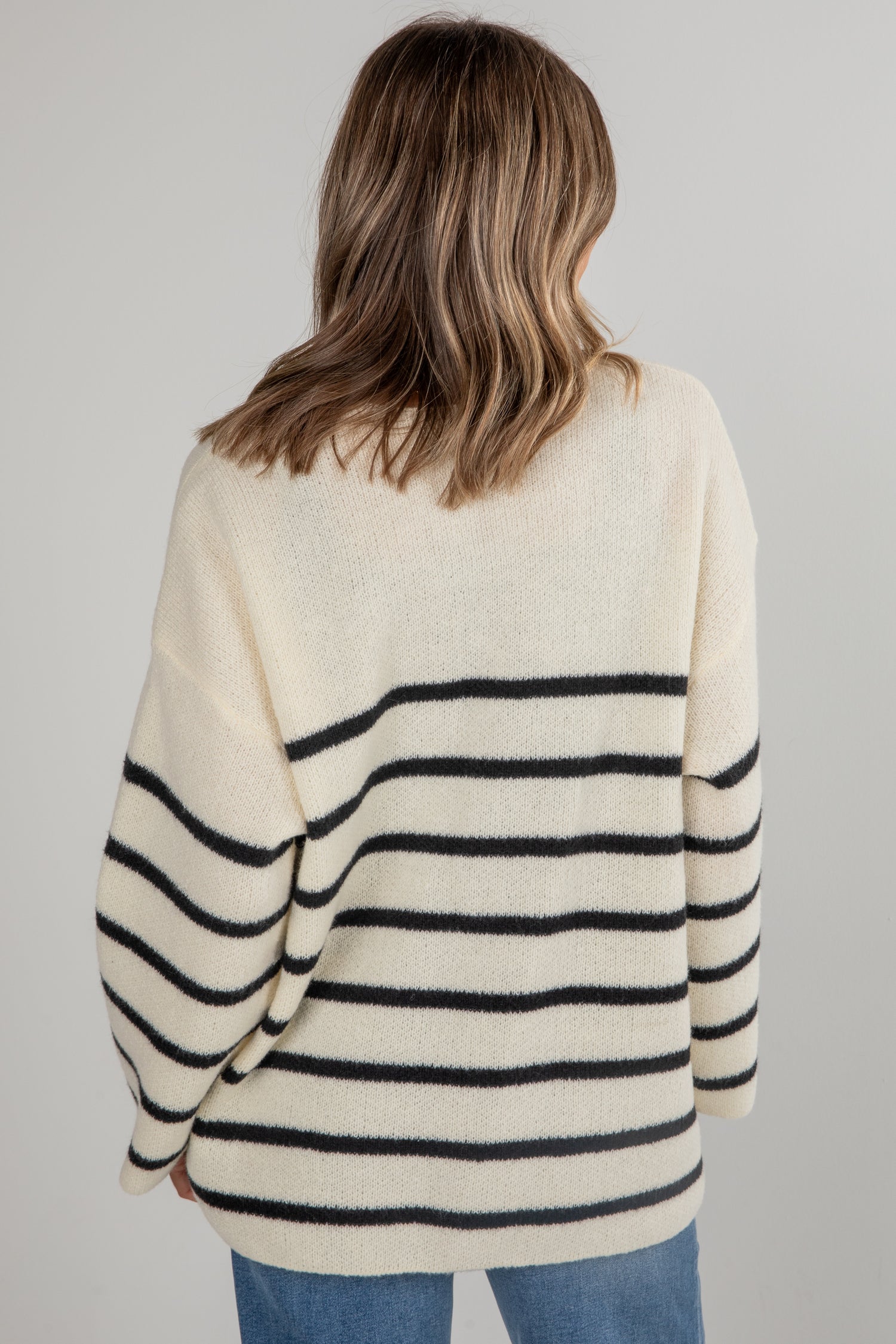 Person wearing a cream sweater with black horizontal stripes on a plain background