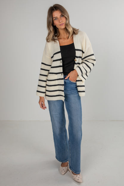 Woman wearing a striped cardigan, black top, and blue jeans on a white background