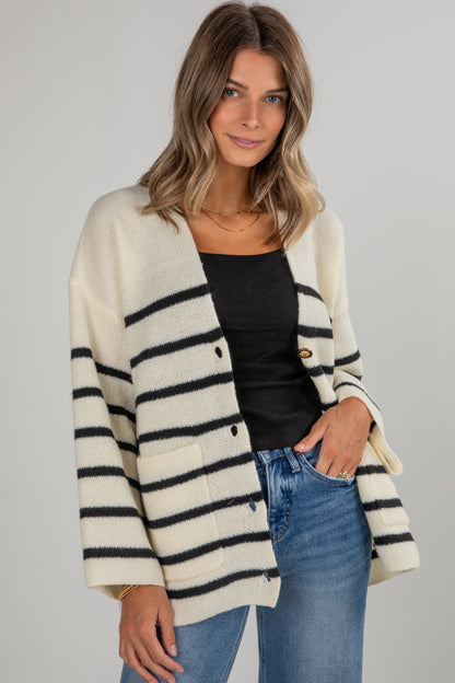 Woman wearing a striped cardigan over a black top and blue jeans on a gray background