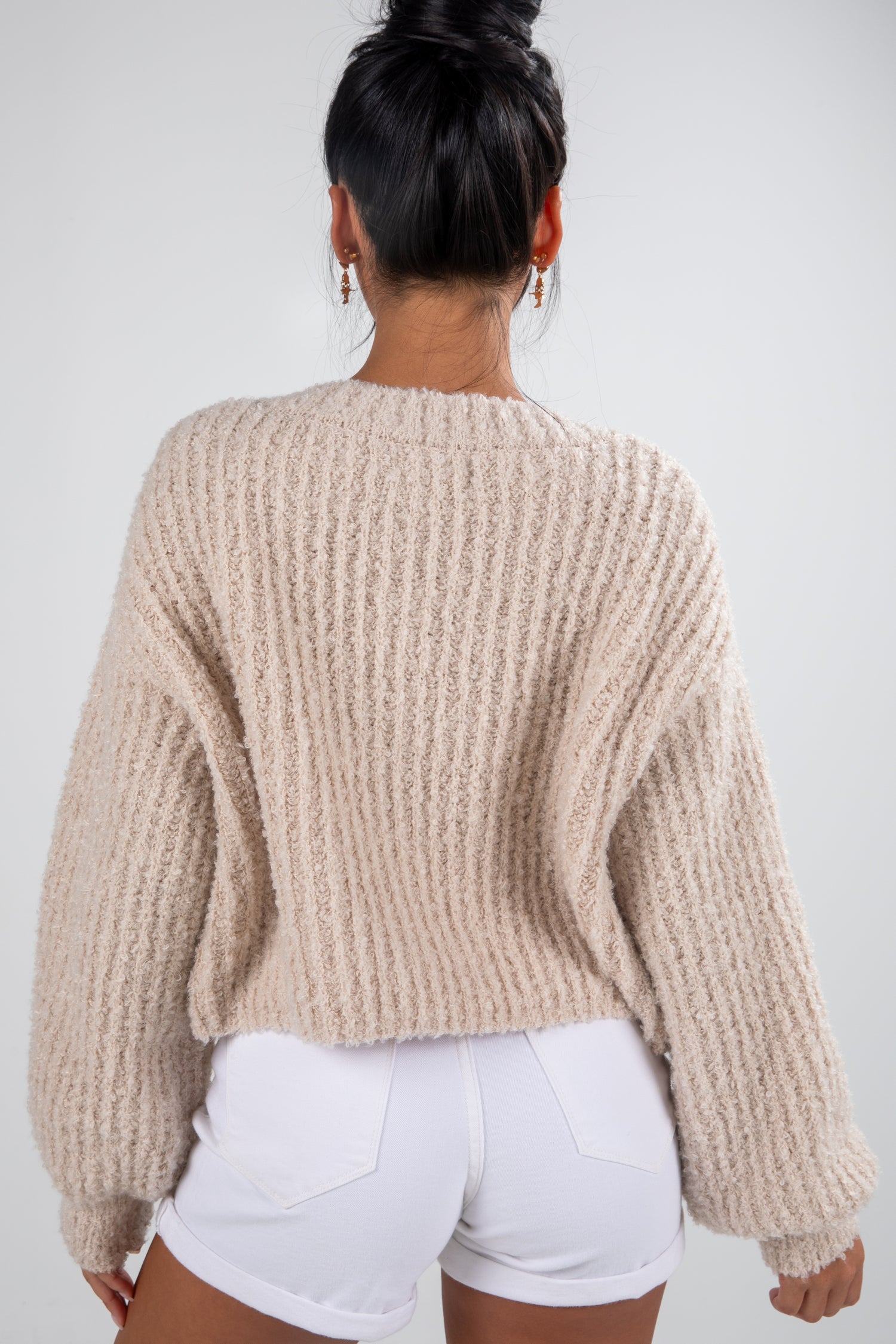 Person wearing a beige chunky knit sweater and white shorts on a plain background