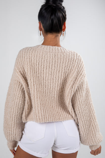 Person wearing a beige chunky knit sweater and white shorts on a plain background
