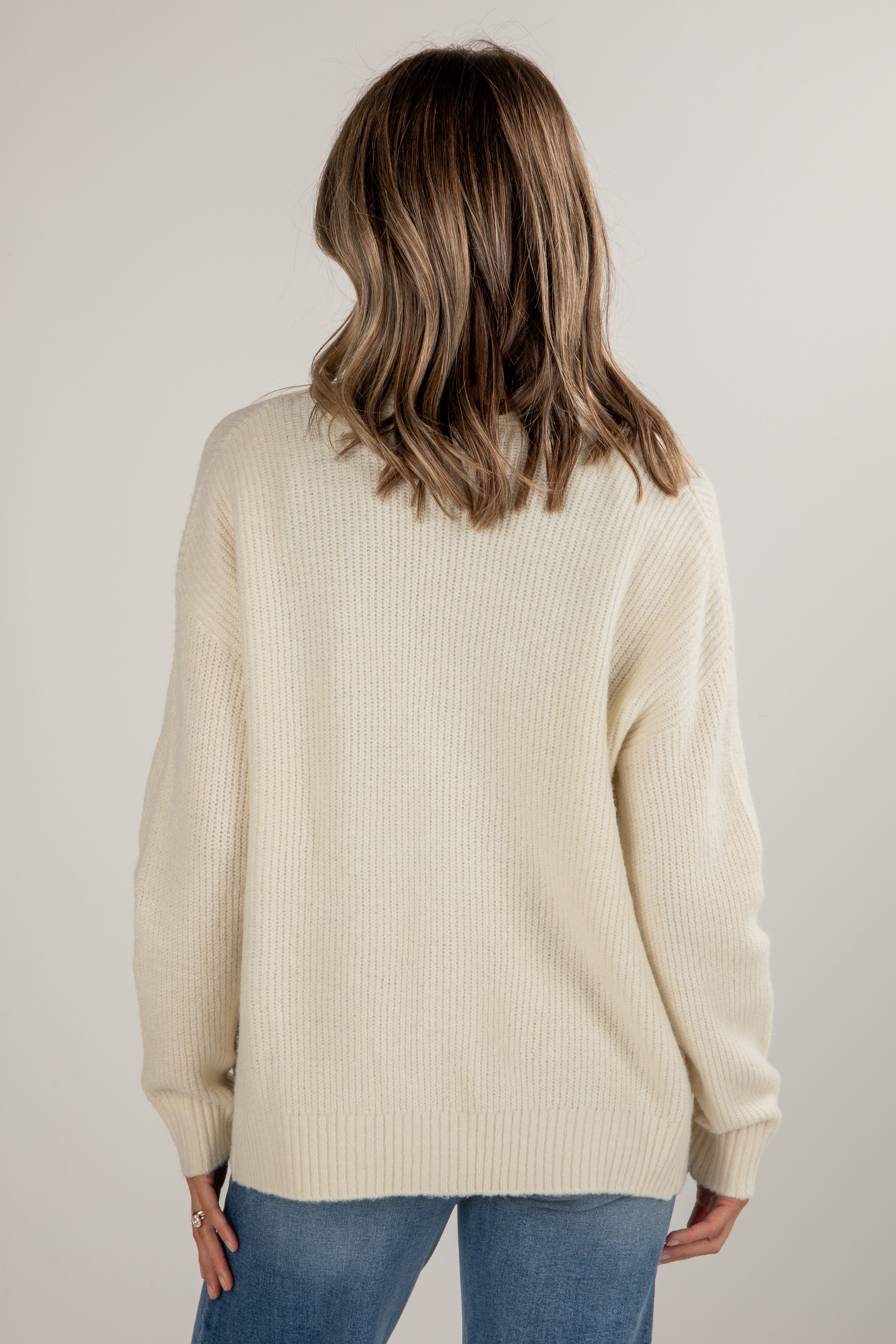 Person wearing a beige sweater and blue jeans against a plain background