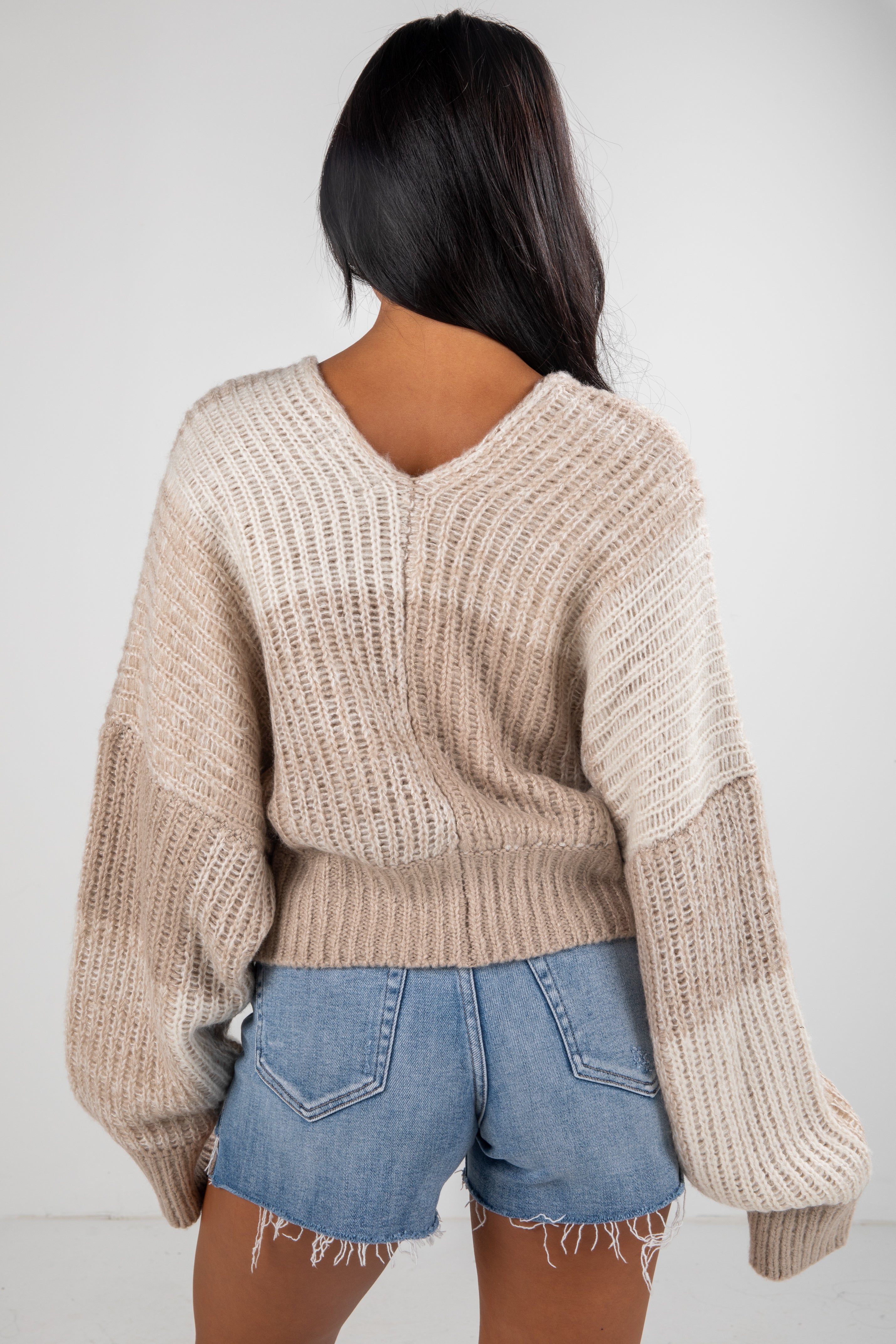 Person wearing a beige knitted sweater and denim shorts on a white background