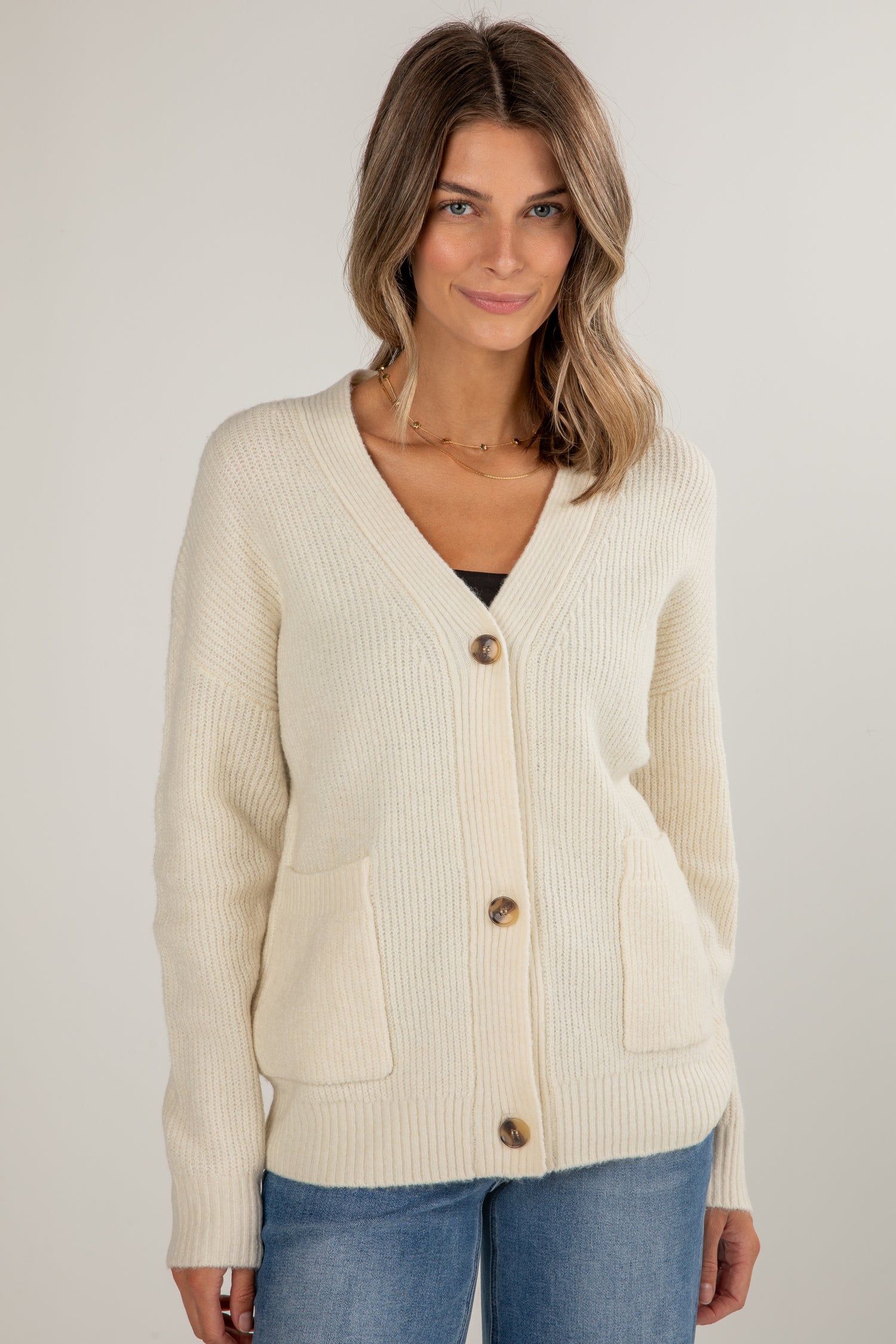 Woman wearing a cream cardigan with buttons on a plain background