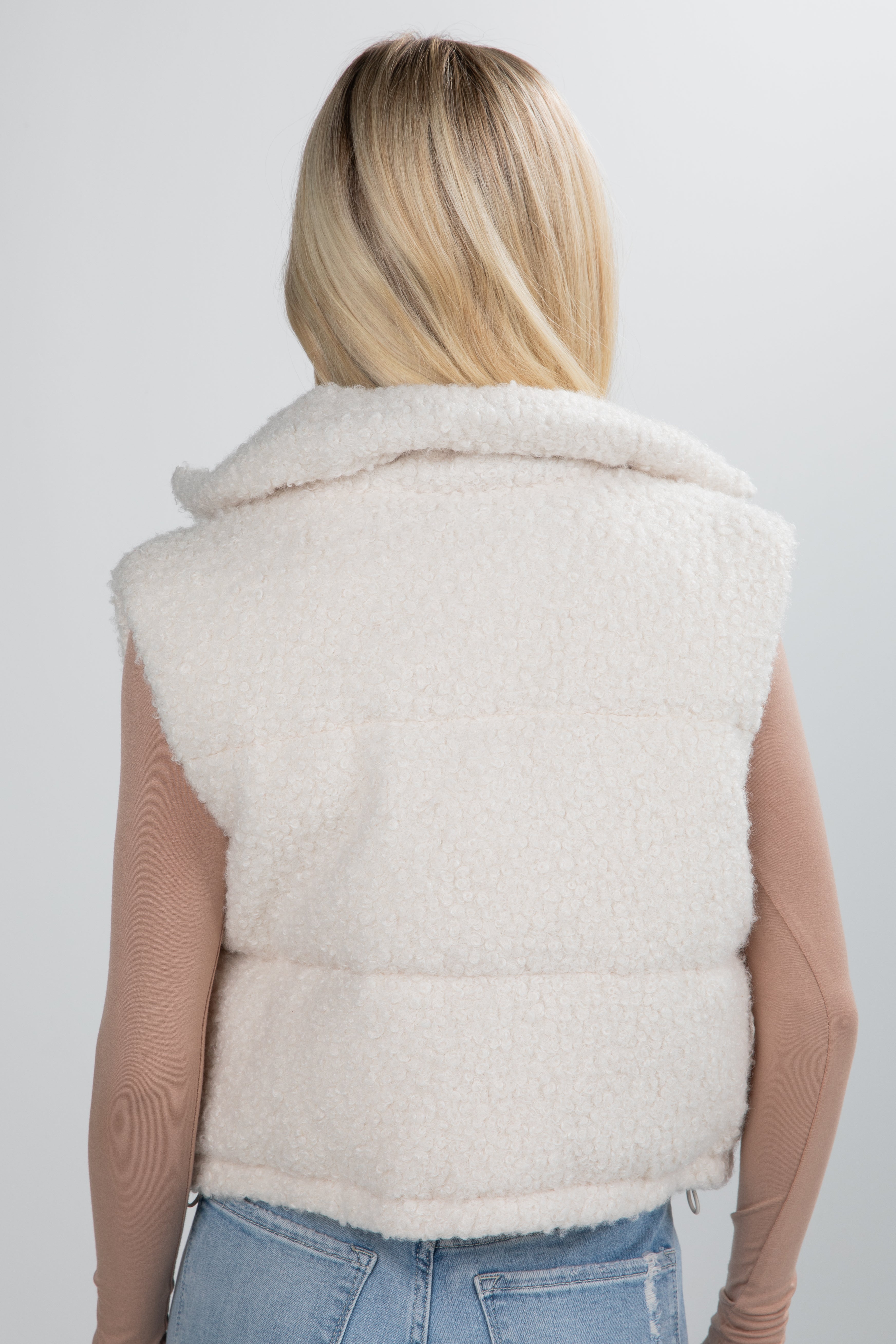 Person wearing a white puffer vest on a plain background