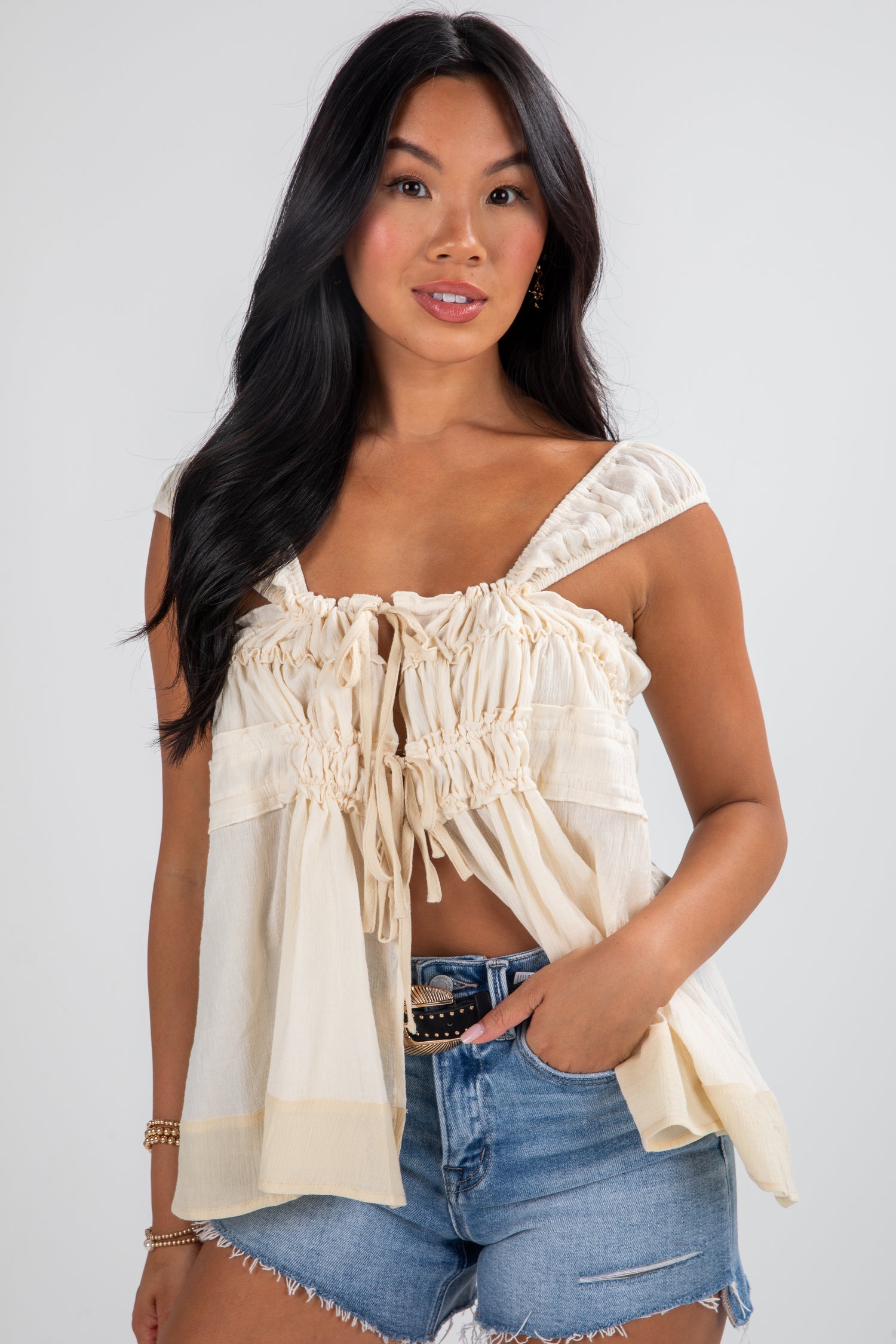 Woman wearing a beige off-shoulder top and denim shorts on a white background