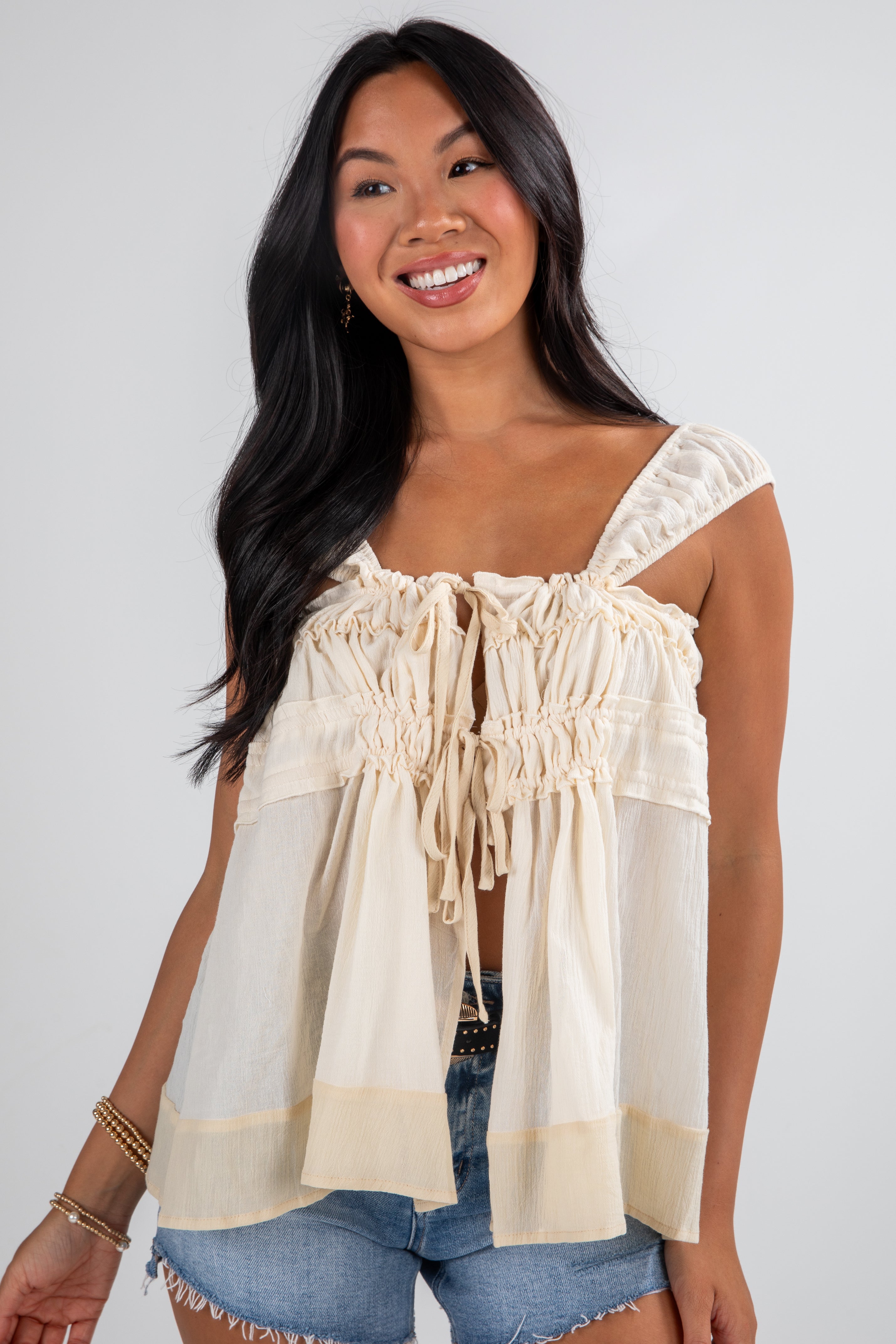 Woman wearing a beige blouse with ruffled details against a white background