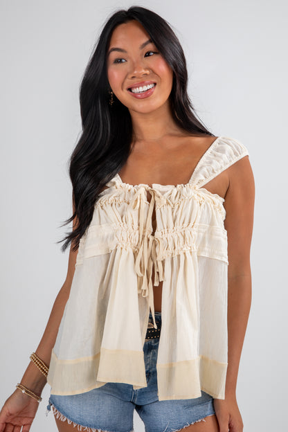 Woman wearing a beige blouse with ruffled details against a white background