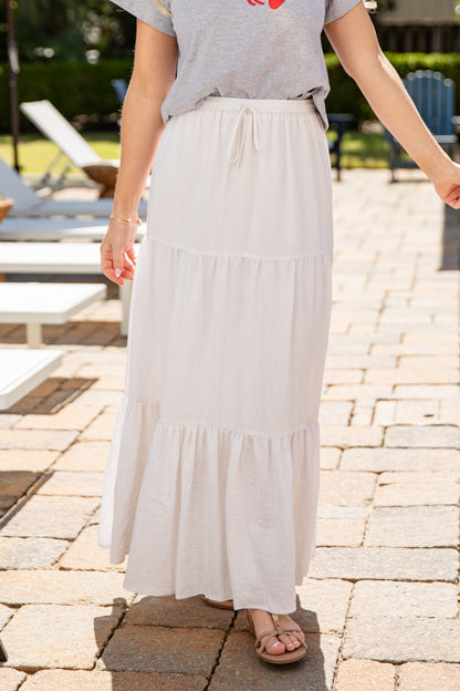 Person wearing a gray t-shirt and white tiered skirt on a paved outdoor area.