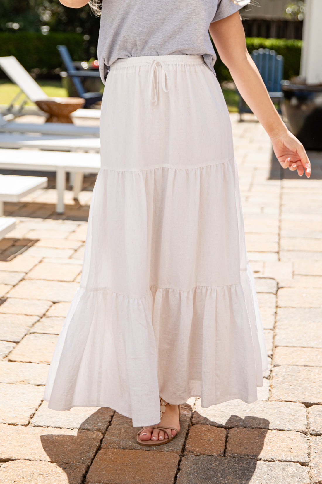 Person wearing a light-colored tiered skirt on a paved outdoor patio.