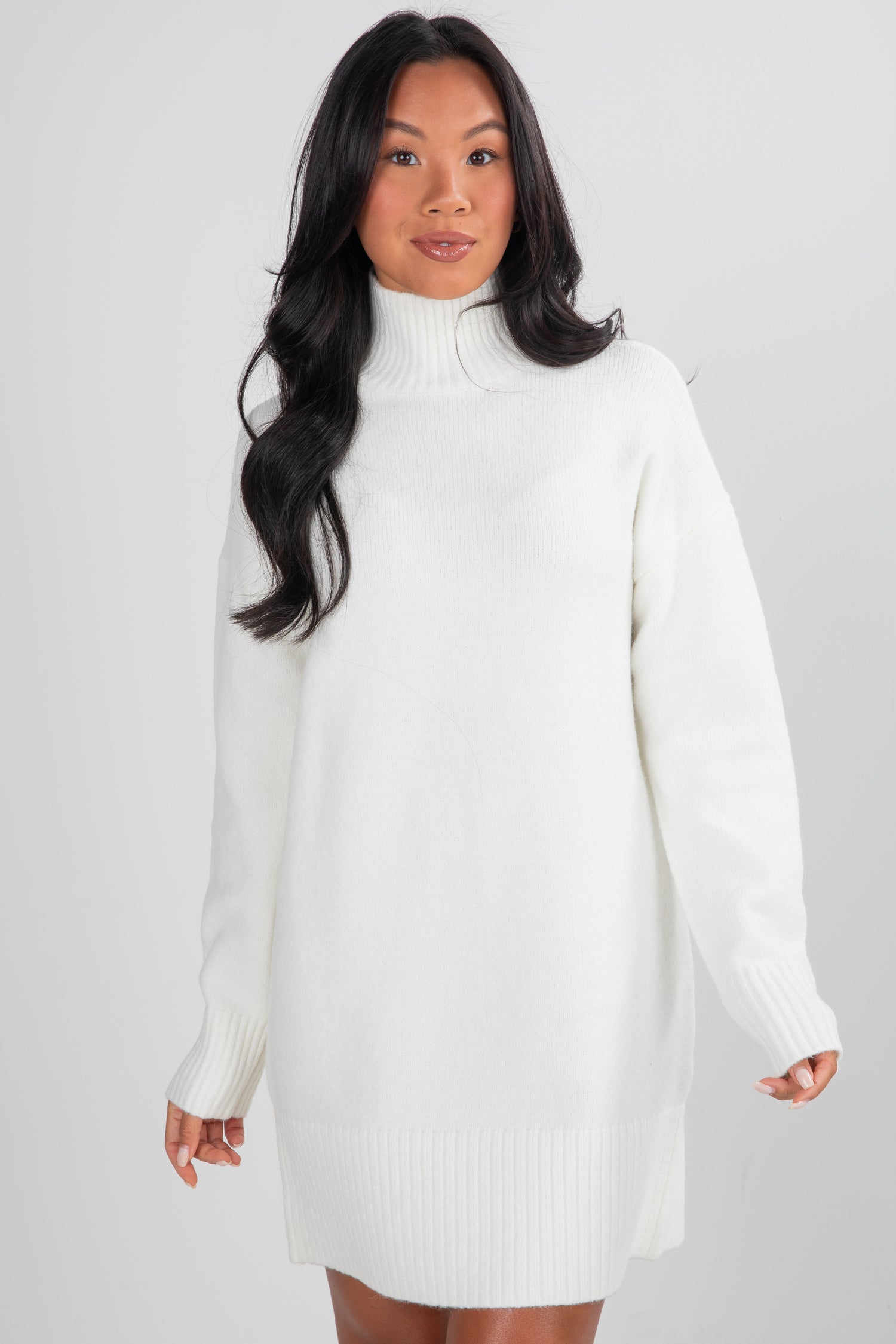 Woman wearing a white sweater dress against a plain background
