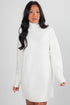 Woman wearing a white sweater dress against a plain background