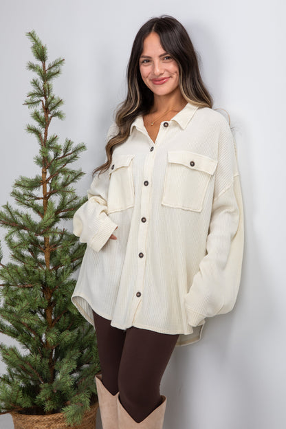 Woman wearing a white shirt standing next to a small Christmas tree against a plain background