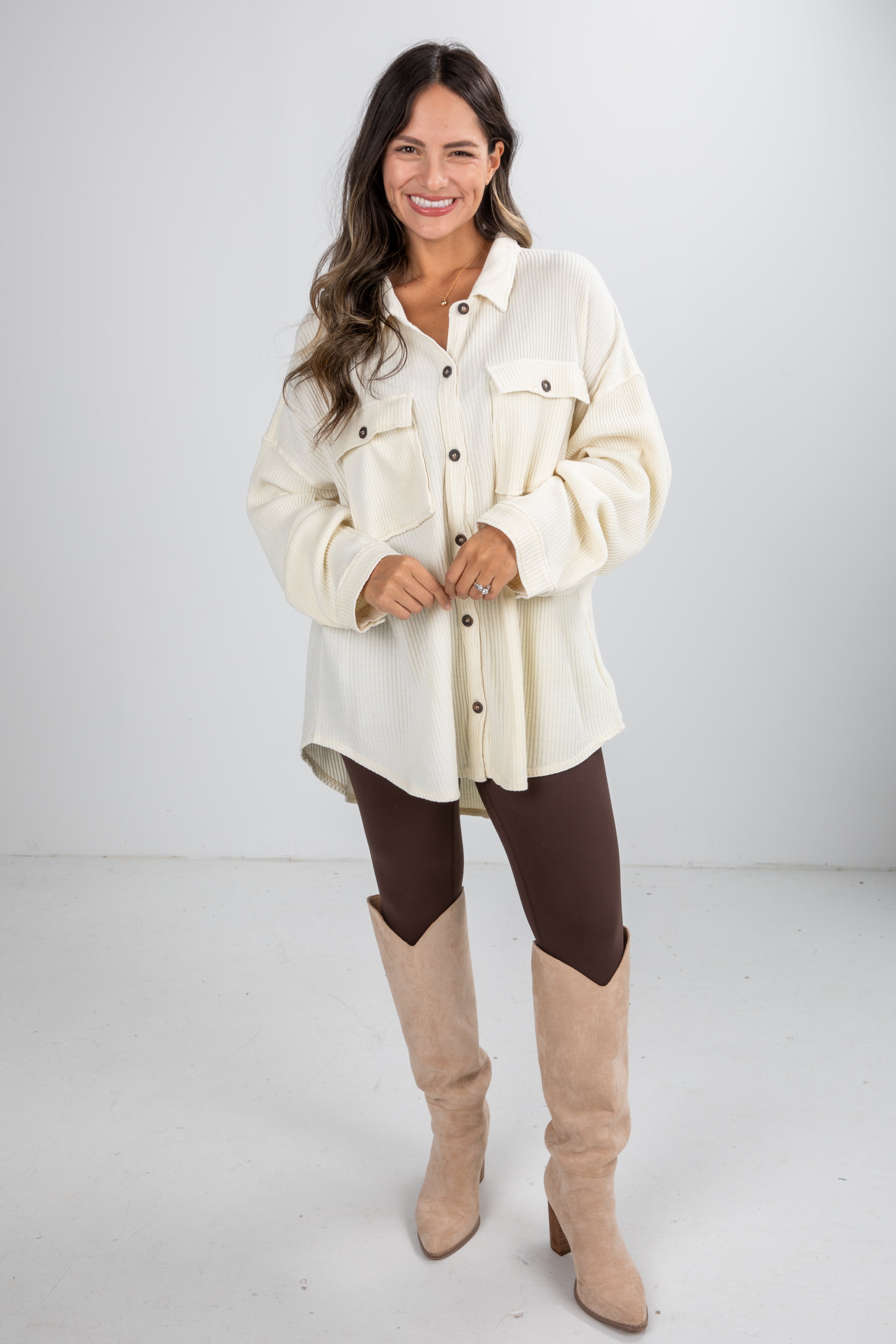 Woman wearing a cream jacket, brown leggings, and beige knee-high boots on a white background