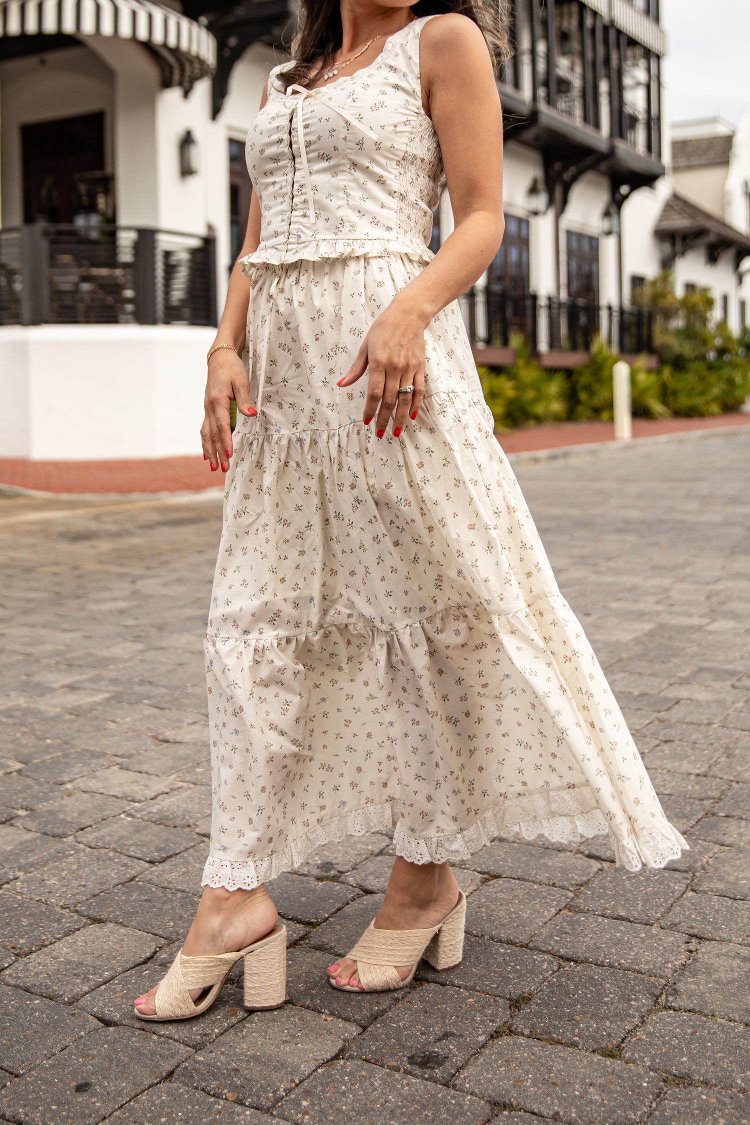 Woman wearing a white floral dress on a cobblestone street.