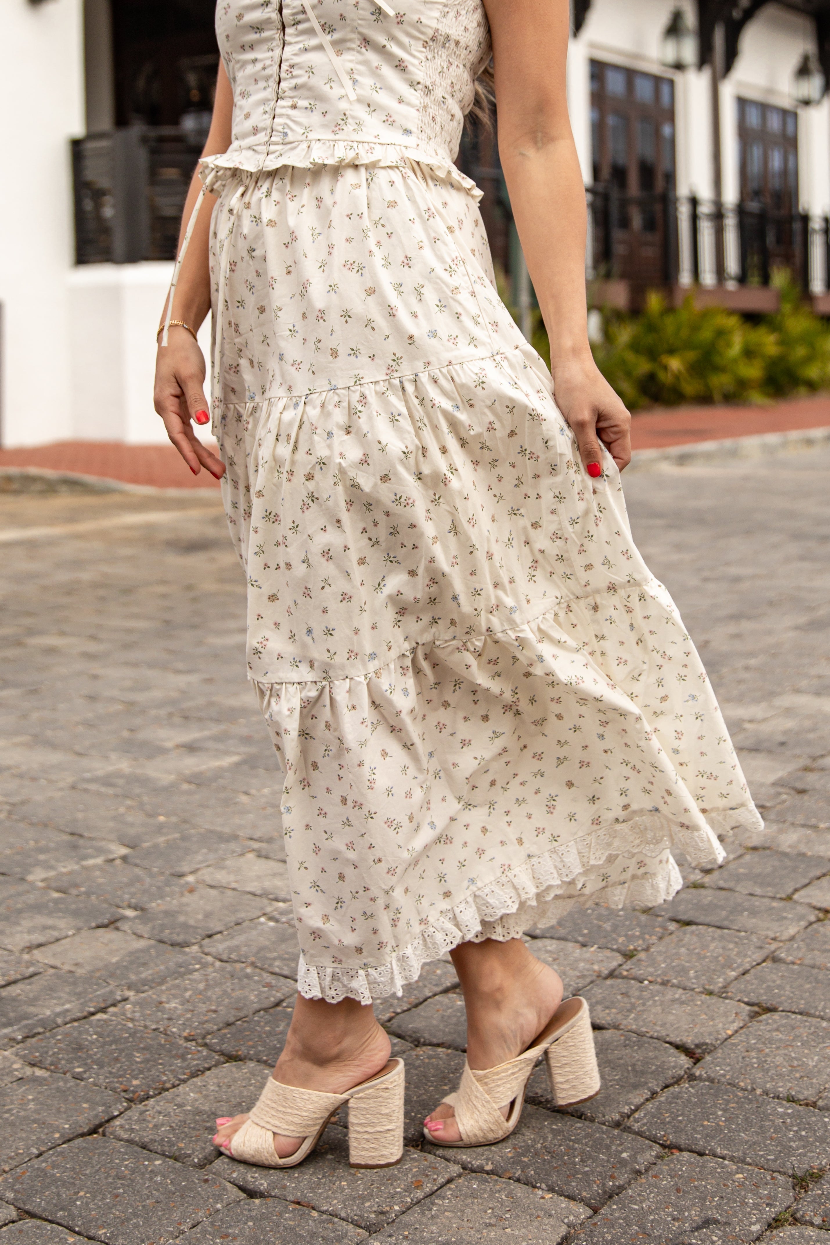 Woman wearing a white floral dress on a paved street.