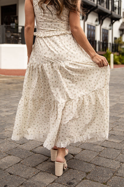 Woman wearing a white floral dress on a cobblestone street.
