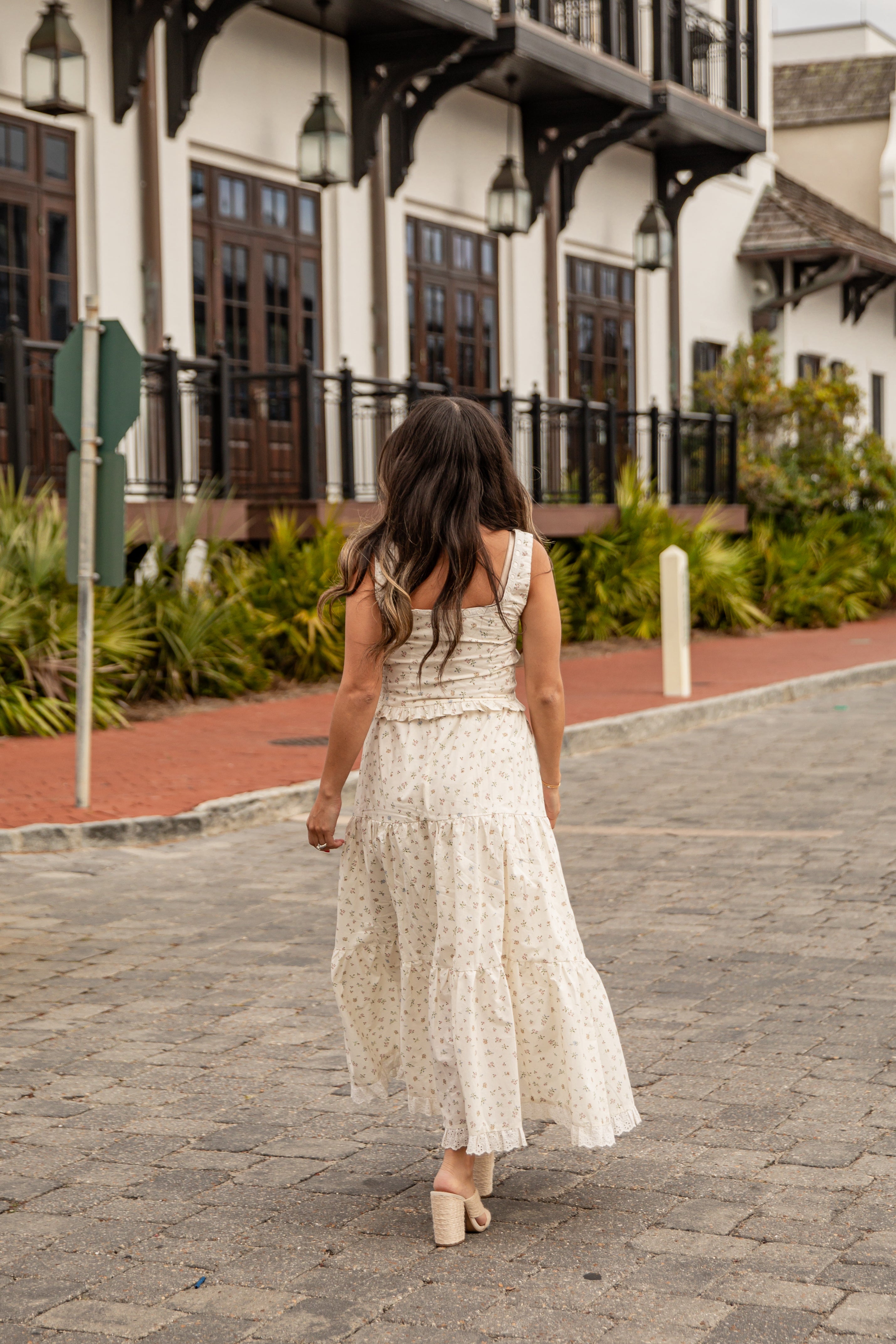 Woman in a white dress walking on a paved path with a building in the background
