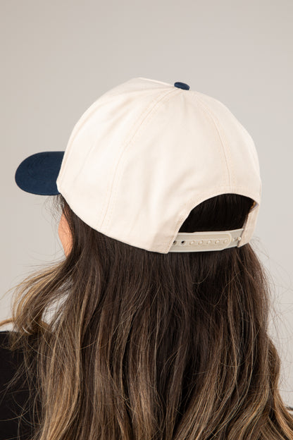 Person wearing a beige cap with a dark blue bill on a plain background