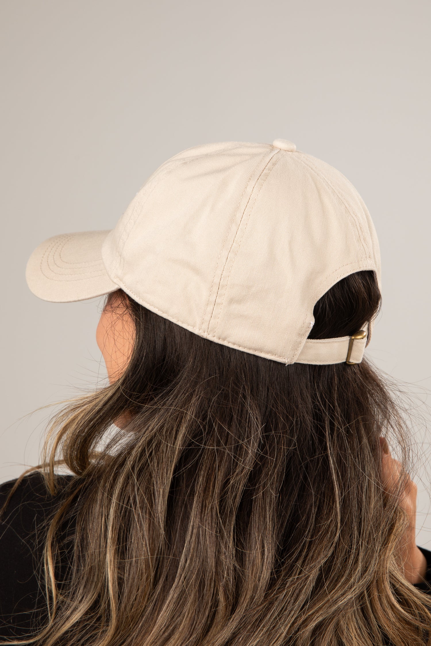 Person wearing a beige baseball cap with black hair peeking out from under it on a plain background