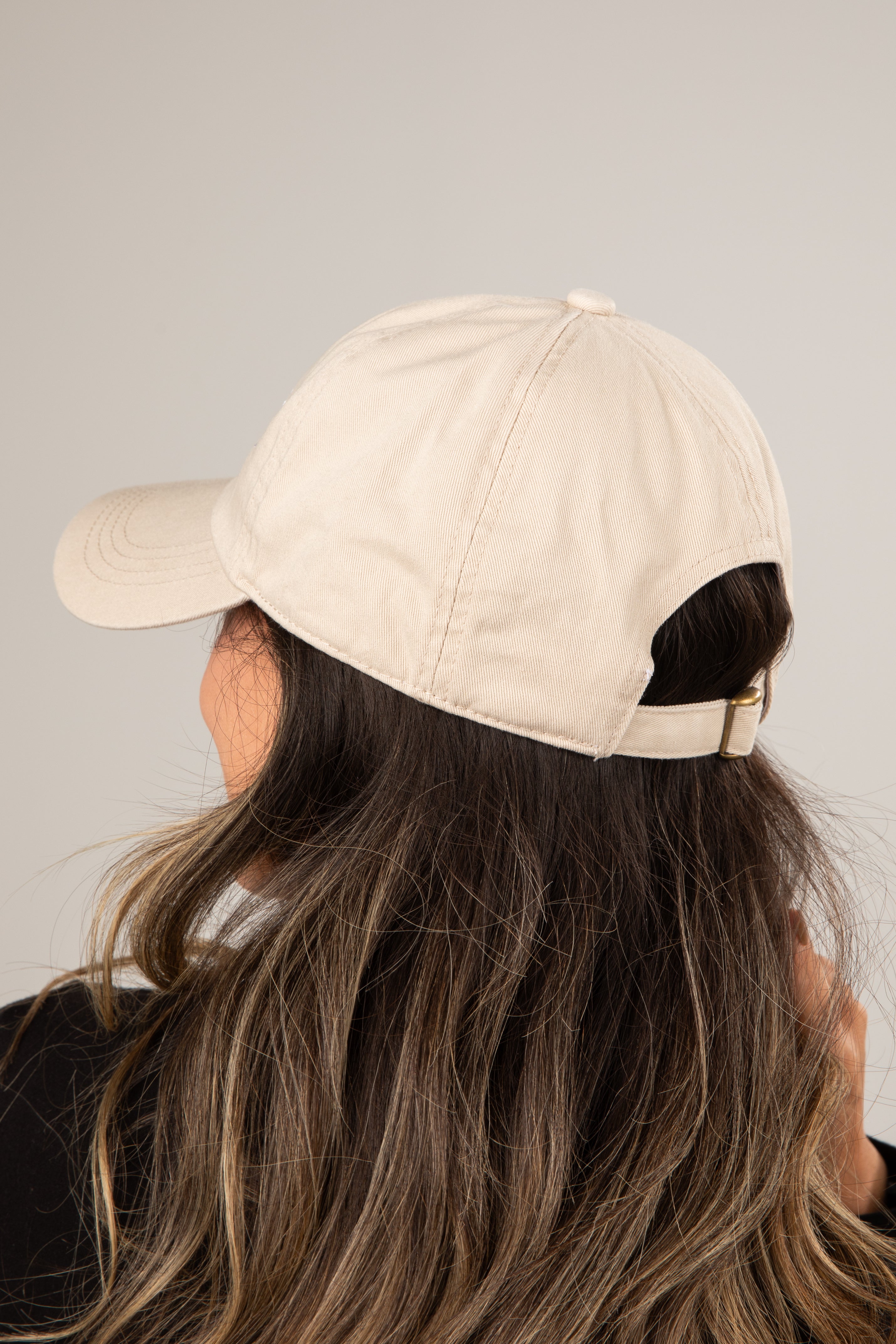 Person wearing a beige baseball cap with black hair peeking out from under it on a plain background