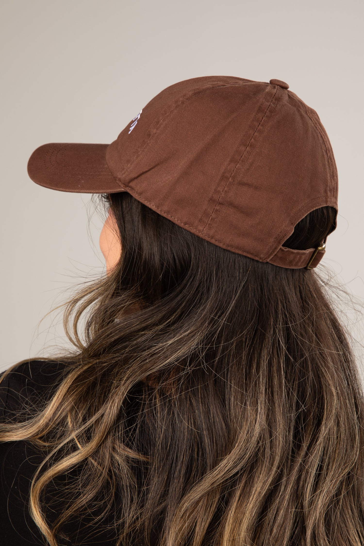 Brown cap worn by a person with long, wavy hair on a neutral background