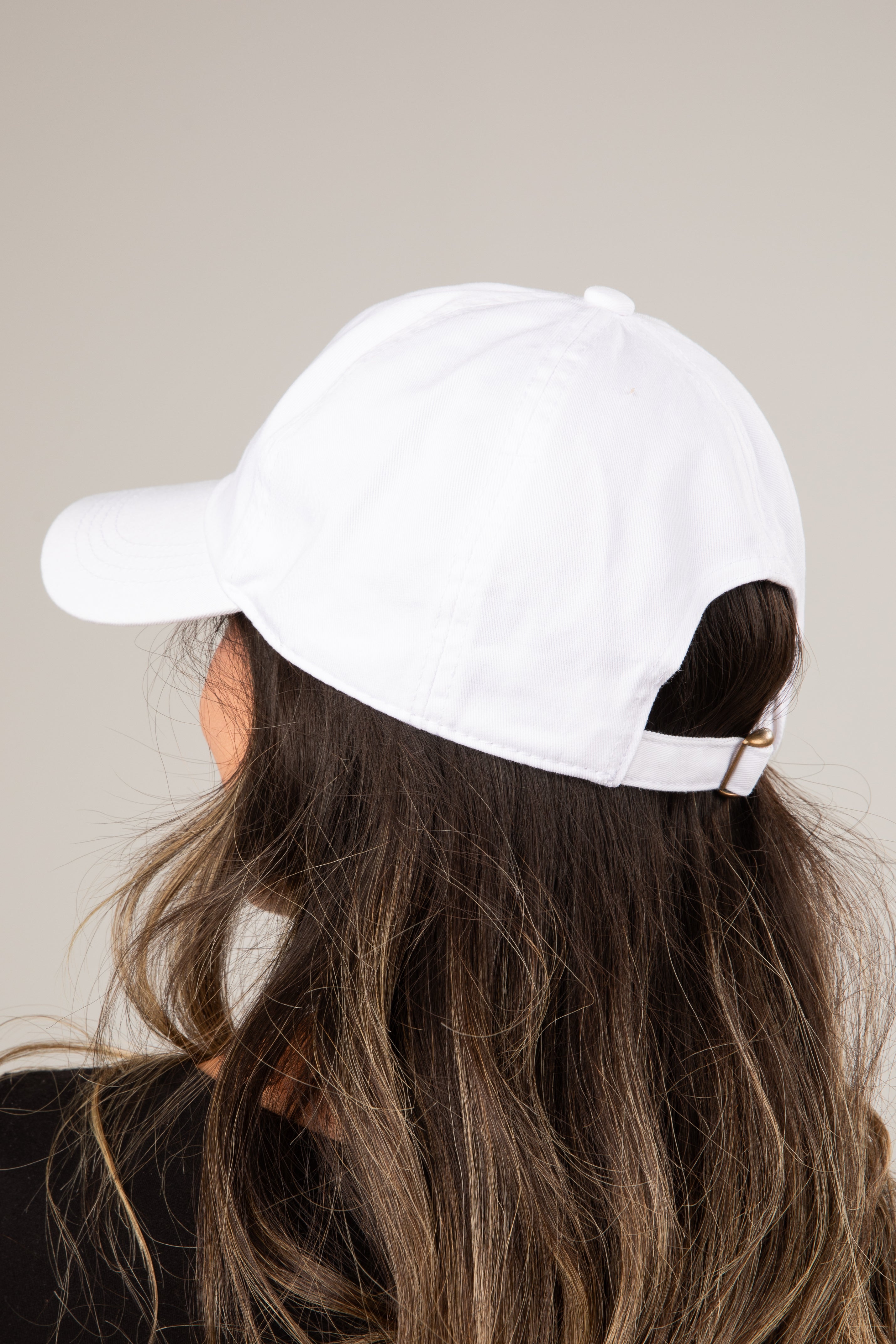 White baseball cap worn by a person with long hair on a plain background
