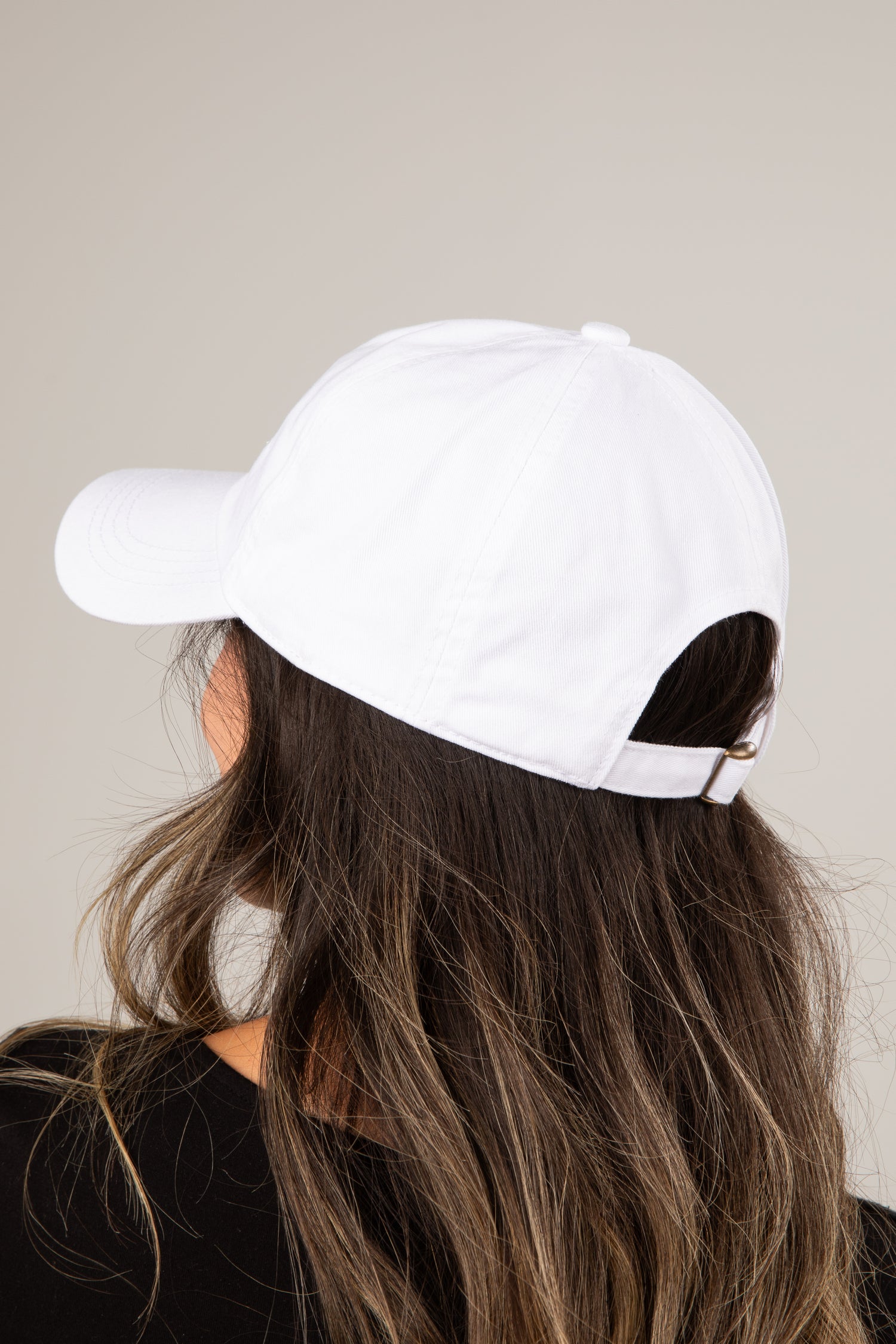 White baseball cap worn by a person with long hair against a neutral background