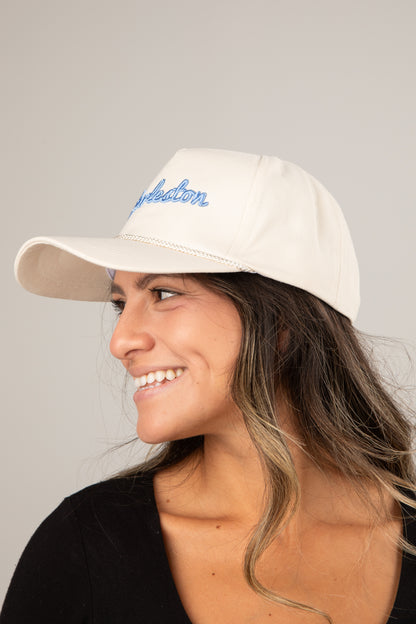Woman wearing a beige cap with blue text on a neutral background