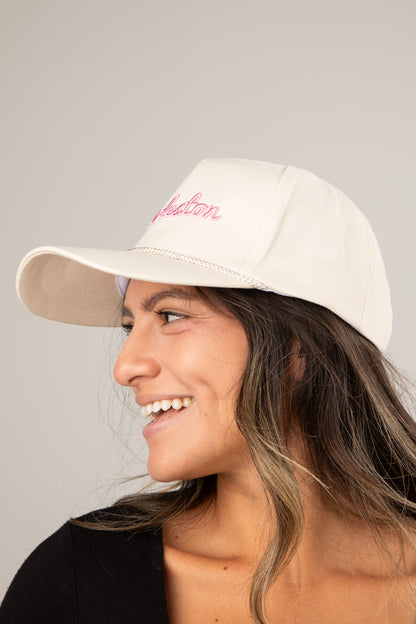 Woman wearing a beige cap with pink text on a gray background