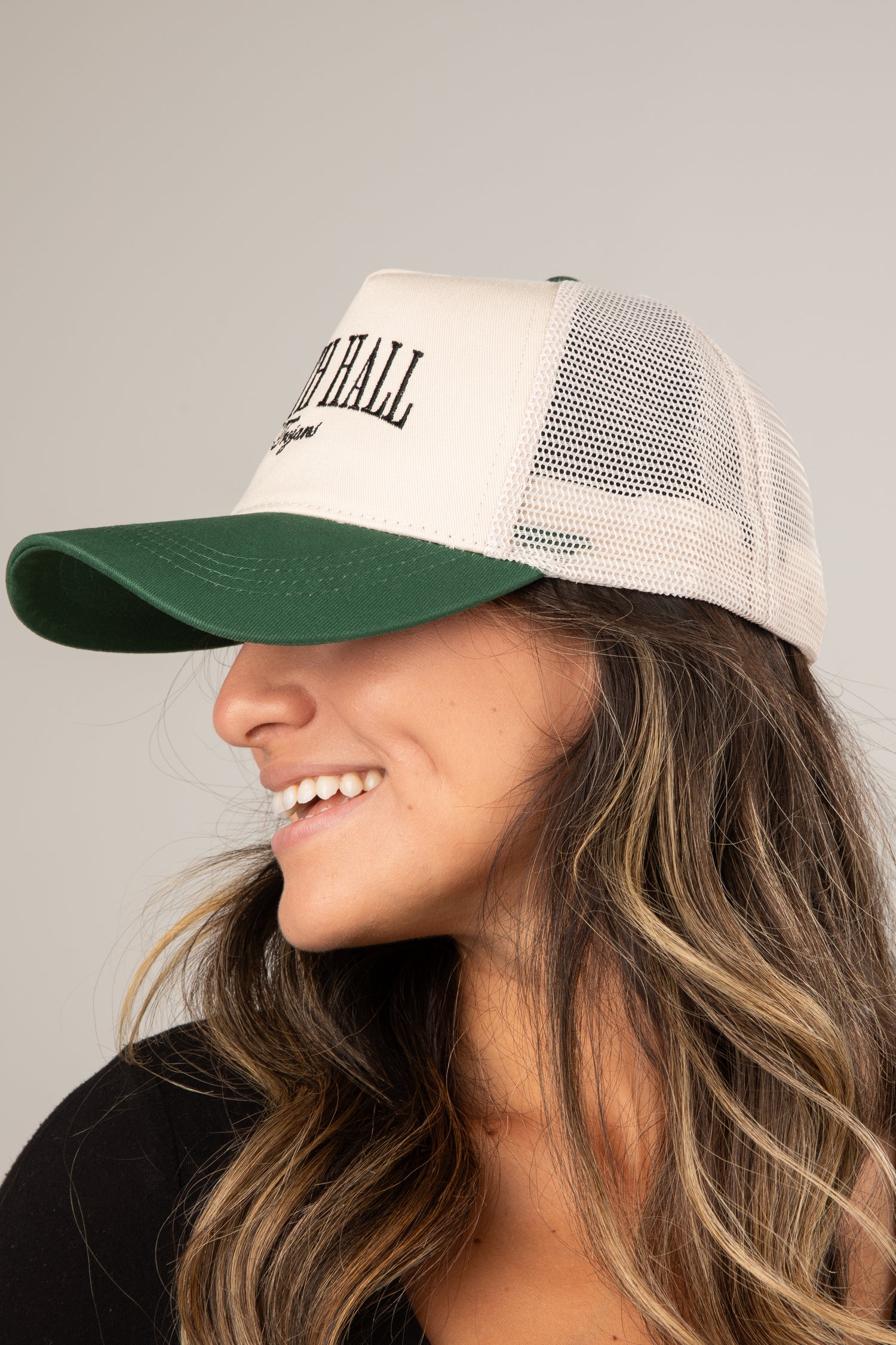 Woman wearing a beige and green cap with mesh back on a gray background