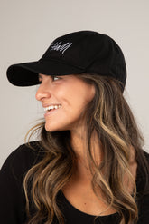 Woman wearing a black cap with white text on a neutral background