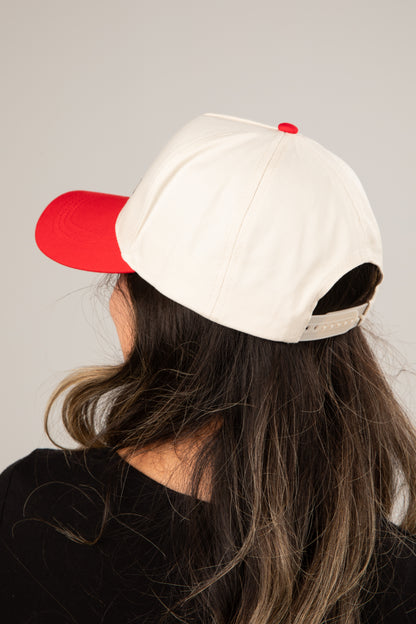 Person wearing a white cap with a red bill on a plain background